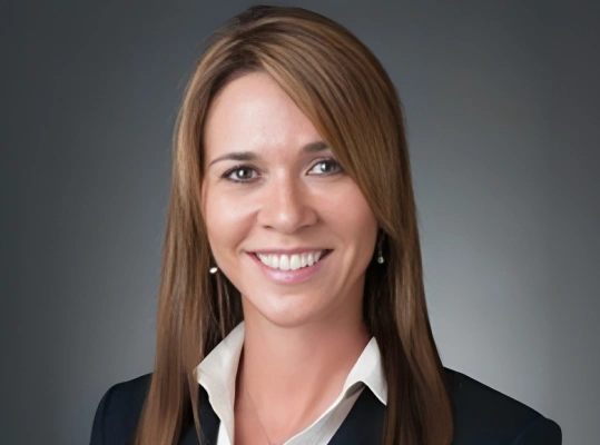 Professional headshot of smiling woman in business attire against gray background.